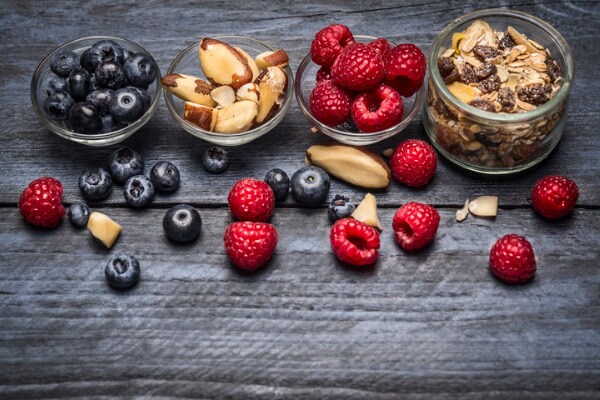 Glasschalen mit Zutaten für ein gesundes Frühstück - Müsli, Beeren und Nüsse auf blauem, rustikalem Holzhintergrund