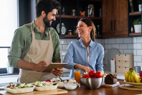 Schönes junges Paar benutzt ein digitales Tablet und lächelt beim Kochen in der Küche zu Hause